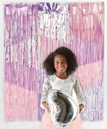 Young woman smiling at camera holding a silver balloon against a pink and purple striped metallic fringe backdrop.