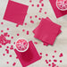 Bright magenta paper napkins arranged on a white wooden surface with pink confetti and two bowls of pink frozen dessert.