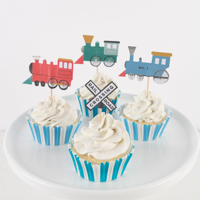 Train Cupcake Kit with frosted cupcakes topped with colorful train engine and railroad crossing decorations in blue and white striped cases.
