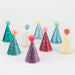 Assorted glitter mini cone party hats in multiple colors including pink, purple, teal, red, yellow, and blue, each topped with a pom-pom.
