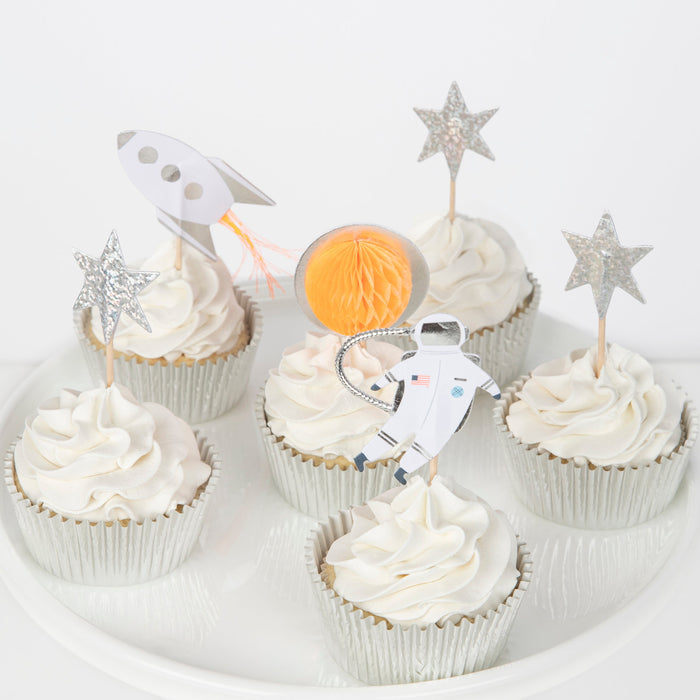 Space Cupcake Kit with frosted cupcakes in silver cases decorated with rocket, astronaut, planet, and glittery star toppers on a white plate.