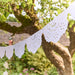 White Lace Style Pennant Garland with scalloped cutout pennants hanging outdoors in a garden setting.
