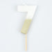White number 7 cake candle with metallic gold dipped finish and wooden pick on a white background.