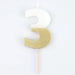 White number 3 cake candle with metallic gold dipped finish and wooden pick on a white background.