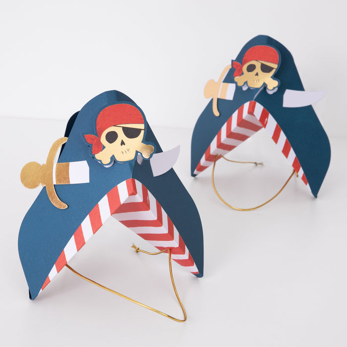 Blue Pirate Party Hats with navy pirate hat shape, red-and-white striped interior, skull and crossbones design, gold sword accent, and elastic cords on a white background