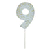 Pale blue number 9 cake candle with gold speckle accents and white pick on a white background.