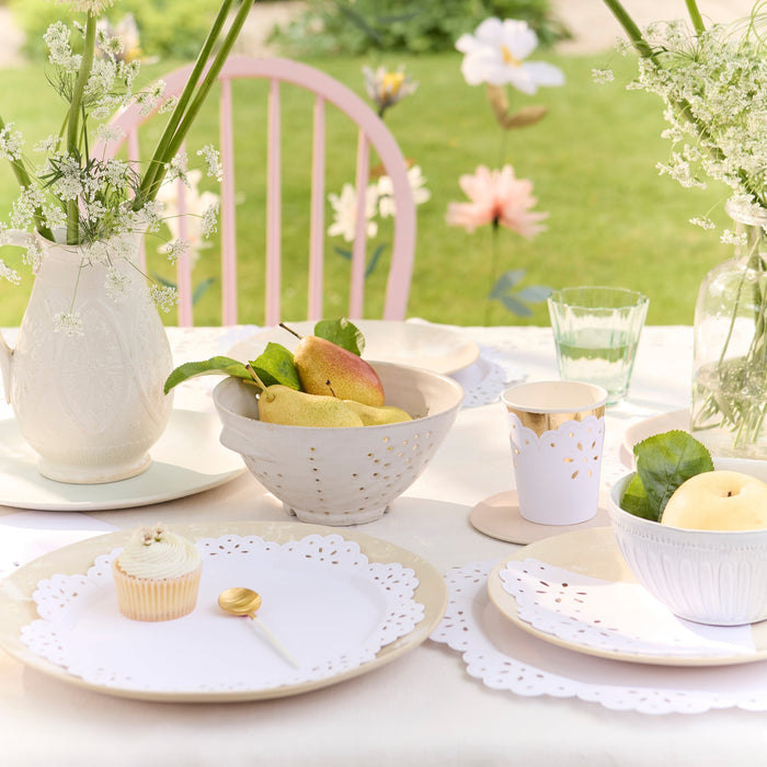 Outdoor table setting with white tableware, fruit, and flowers in a garden.