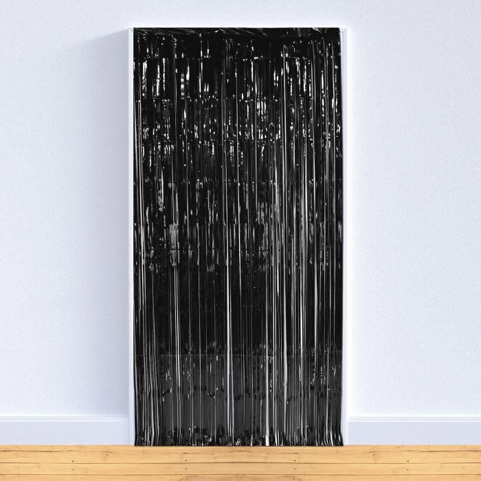 Black metallic fringe curtain with vertical strands hanging from a white header strip, displayed leaning against a white wall on a wooden floor.