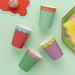 Colorful paper cups in red, green, purple, and mint green with white scalloped trim arranged on a pale green background.