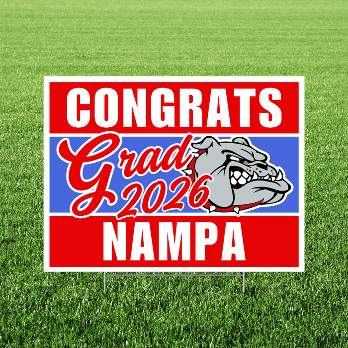 Red, white, and blue yard sign with "Congrats Grad 2026 Nampa" text and a bulldog mascot head in the center, displayed on grass.