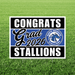 Yard sign with black and white borders framing a blue center section reading "CONGRATS Grad 2026" with a North Mesquite Stallions horse logo, displayed on grass.