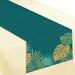 Teal table runner with gold and blue tropical palm leaf and monstera leaf designs displayed diagonally on a cream background.