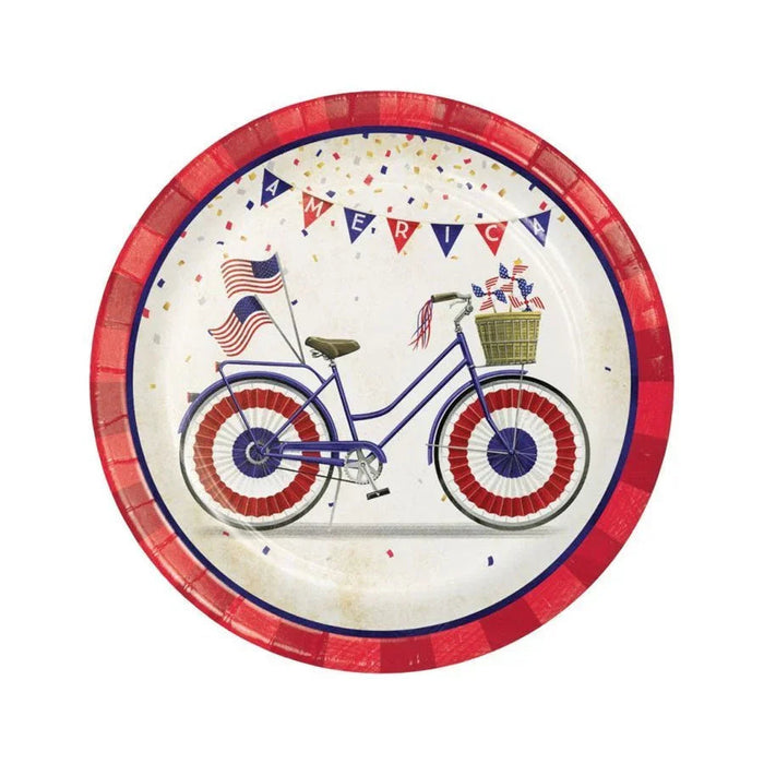 Red paper dessert plate featuring a blue bicycle decorated with American flags and a basket, surrounded by patriotic bunting and confetti on a cream background.