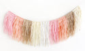 Curved tissue paper fringe garland with layered strips in shades of pink, coral, cream, tan, and white creating an ombré effect.