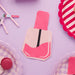 Bright pink nail polish bottle-shaped paper napkins arranged on a lavender background with coordinating party decorations including striped and checkered patterns.