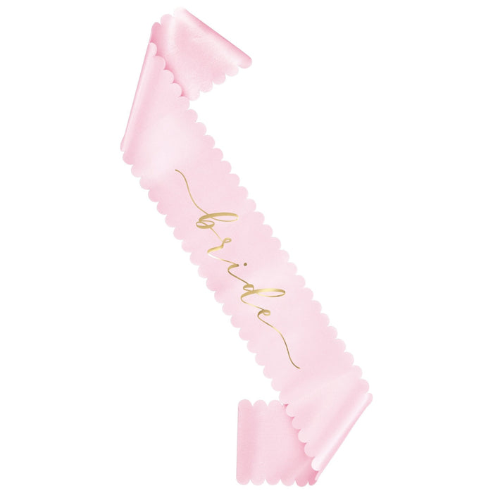 Pink sash with scalloped edges and gold script text reading "Bride" displayed diagonally against a white background.
