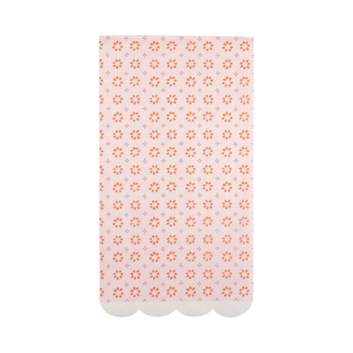 Pink napkin with repeating orange floral and geometric pattern design and white scalloped edges along the bottom.