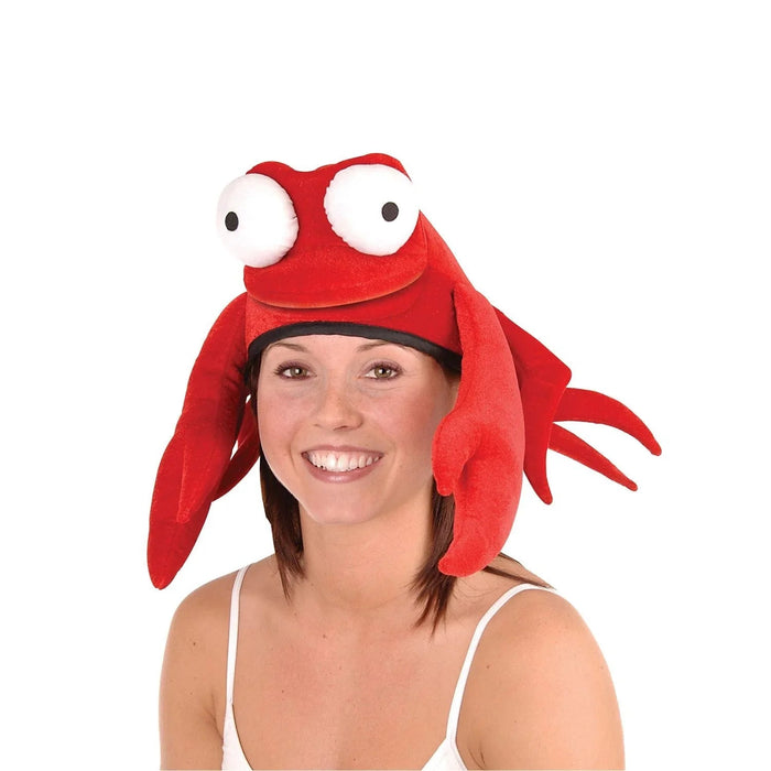 Bright red plush crab hat with oversized white and black eyes, red claw-shaped ear flaps, and a wide smiling mouth, worn by a smiling woman against a white background.