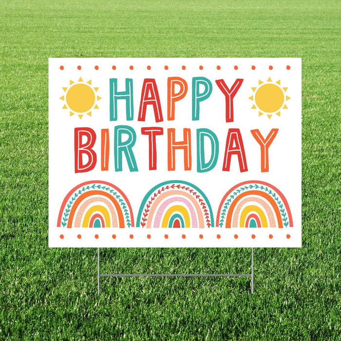 Colorful yard sign with "Happy Birthday" text in red, teal, and orange letters, decorated with yellow suns and three rainbow designs with leaf accents on a white background.