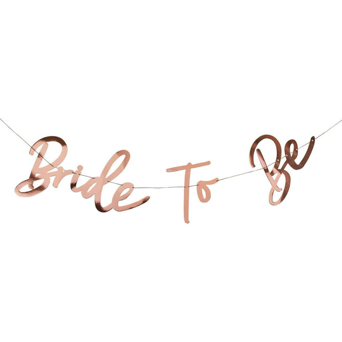 Rose gold metallic banner with cursive lettering reading "Bride to Be" connected by string.