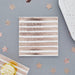 Rose gold foil striped napkins arranged on a gray surface with decorative stars and pastry elements around them.