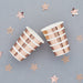 Two rose gold and white striped paper cups surrounded by rose gold star decorations on a gray background.