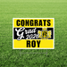 Yellow and black yard sign with "CONGRATS Grad 2026 ROY" text and Royal Royals school crest, displayed on grass.