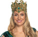 Gold ornamental headpiece featuring two curved snake heads with emerald green jeweled accents, worn by a woman with long blonde hair.
