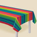 Colorful striped tablecloth with serape-inspired rainbow pattern in teal, magenta, yellow, and green draped over a white table leg against a cream background.