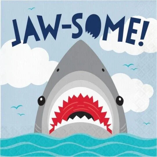Illustrated napkin package featuring a gray shark with open red mouth emerging from turquoise waves against a blue sky with white clouds and "JAW-SOME!" text at the top.