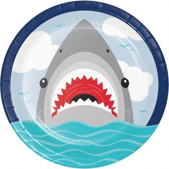 Round paper plate with a shark illustration featuring red spiky teeth, gray body, and turquoise ocean waves at the bottom against a blue sky with white clouds.