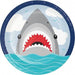 Round paper plate with a shark illustration featuring red spiky teeth, gray body, and turquoise ocean waves at the bottom against a blue sky with white clouds.