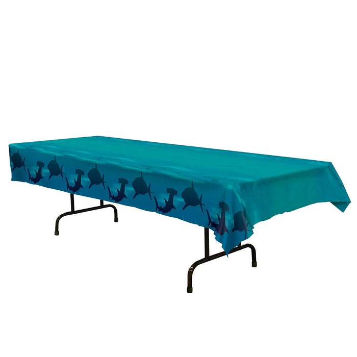 Teal plastic tablecloth featuring a repeating pattern of dark blue shark silhouettes along the bottom border, displayed draped over a black folding table.