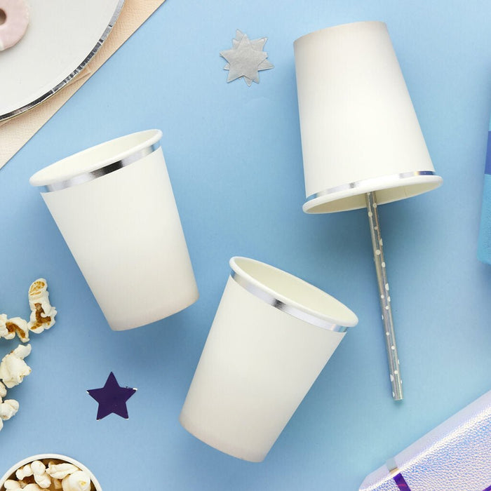 Three white paper cups with silver metallic trim arranged on a blue background alongside decorative stars and popcorn.