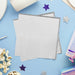 Stack of white napkins with silver gray ombre edges surrounded by purple and white stars, popcorn, and colorful party decorations on a blue background.