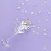 Silver ring-shaped confetti pieces with bow tie details scattered across a purple background and overflowing from a clear martini glass.