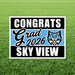 Lawn yard sign with black and white text reading "CONGRATS Grad 2026 SKY VIEW" with a blue wildcat mascot logo in the center, displayed on grass.