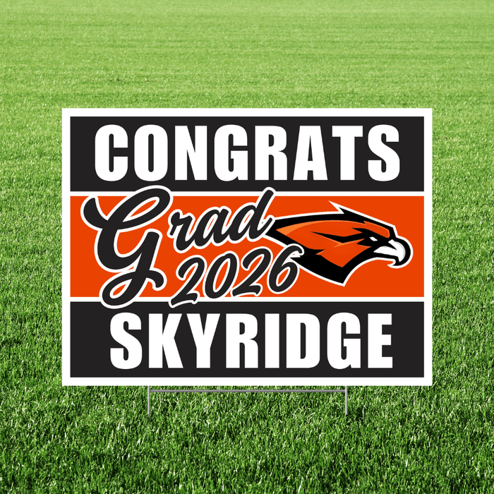 Rectangular yard sign on green grass with black and white border, orange center band featuring a red eagle logo, and text reading "Congrats Grad 2026 Skyridge" in white and script lettering.