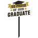 Black and gold plastic yard sign with a graduation cap and banner reading "So Proud of Our Graduate," mounted on a black stake.