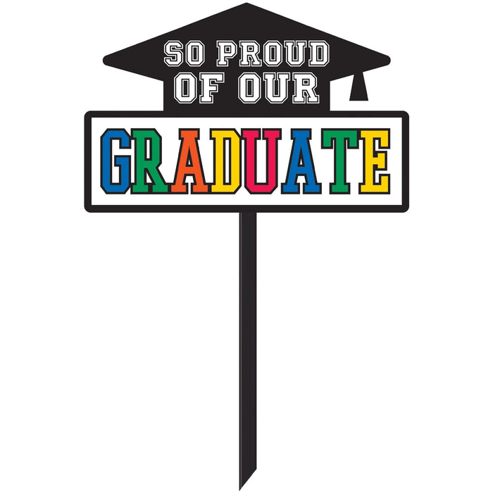Black graduation cap yard sign with multicolor letters spelling "GRADUATE" and white text reading "SO PROUD OF OUR" above it.
