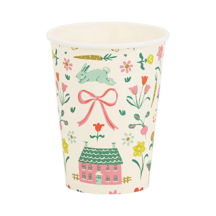Cream-colored disposable cup printed with spring-themed illustrations including a pink cottage with green roof, pink bow, hopping rabbit, colorful flowers, and garden vegetables.