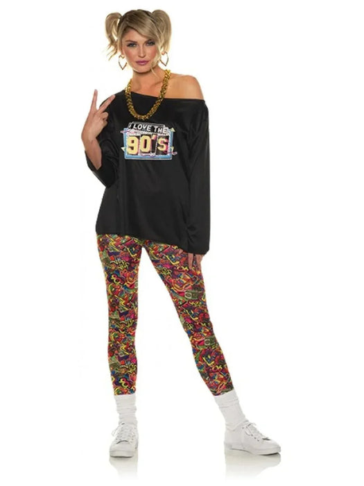 Woman wearing a black off-shoulder sweatshirt with "I Love the 90s" graphic, colorful patterned leggings, white socks, and white sneakers, with blonde pigtails and gold chain necklace.