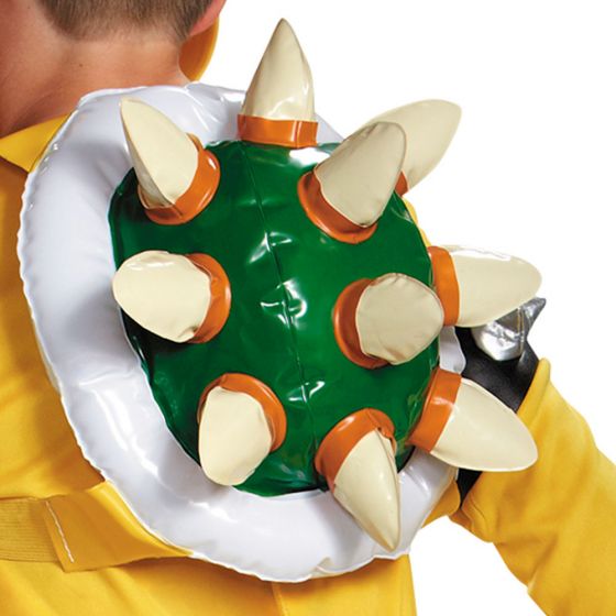Child wearing a green shell costume with cream-colored spikes trimmed in orange, white undershirt, and yellow sleeves, held up by an adult.