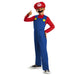 Child wearing a Mario costume with a red cap featuring an M logo, blue overalls with yellow buttons, and red long sleeves.