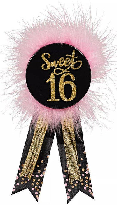 Black circular badge with gold glitter "Sweet 16" text surrounded by pink feather fringe and two black ribbons with gold trim and rhinestone details.