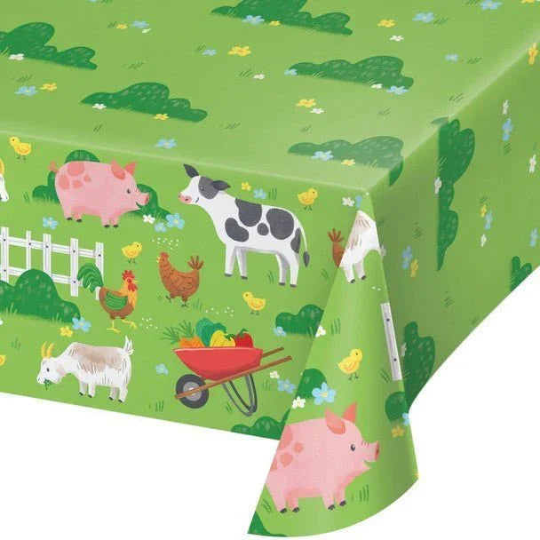 Green paper tablecloth featuring colorful farm animals including pigs, cows, chickens, goats, and a wheelbarrow of vegetables with white picket fence design.