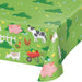 Green paper tablecloth featuring colorful farm animals including pigs, cows, chickens, goats, and a wheelbarrow of vegetables with white picket fence design.