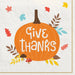 White napkin featuring a large orange pumpkin with "Give Thanks" text, surrounded by autumn leaves, acorns, mushrooms, and colorful stars in fall colors.
