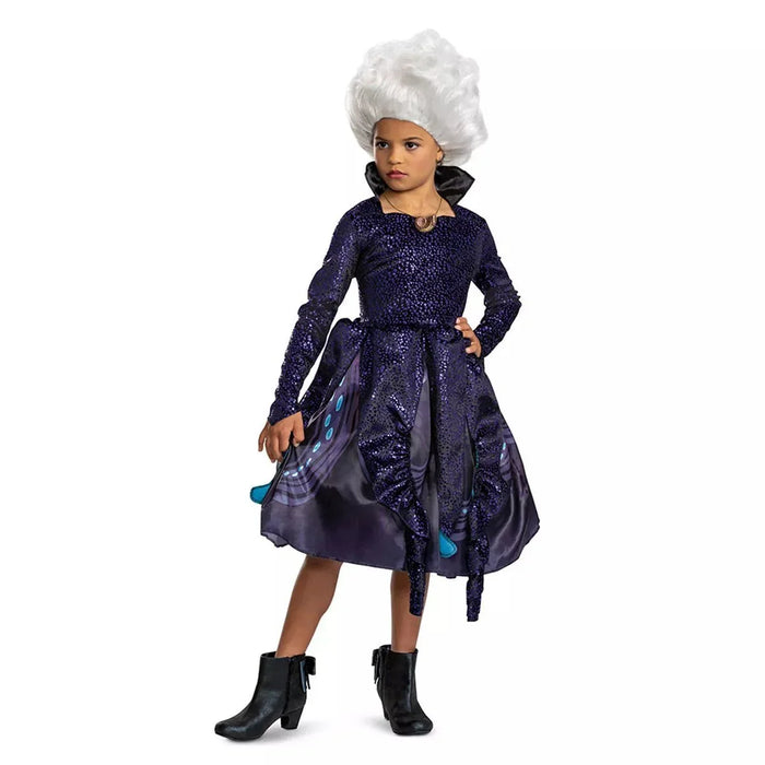 Child wearing a dark purple sequined dress with black satin skirt overlay, black boots, a black high collar, and a white voluminous wig styled upward.