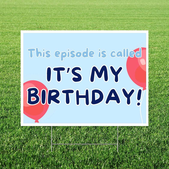 Light blue yard sign with dark blue text reading "IT'S MY BIRTHDAY" and red balloons in the corners, mounted on stakes in grass.